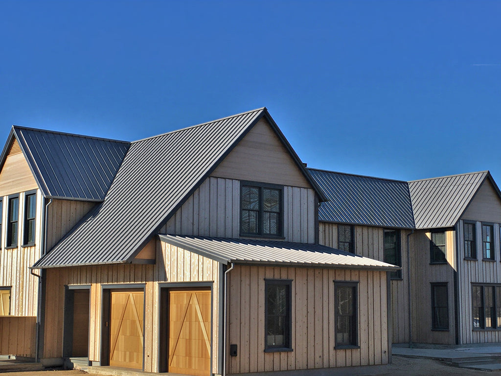 Modern house with dark gray standing seam metal roof panels installed on a steep roof