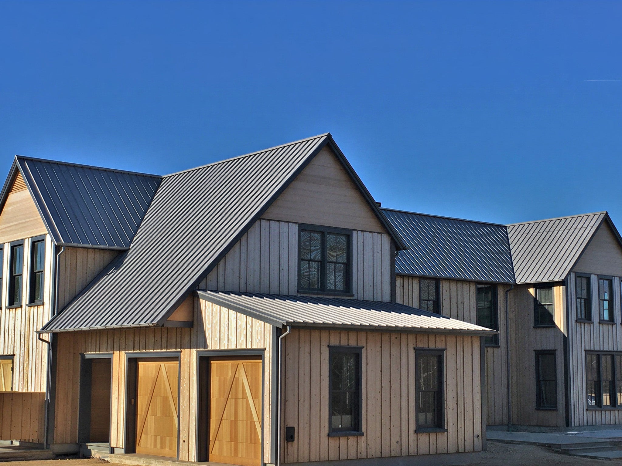 Modern house with dark gray standing seam metal roof panels installed on a steep roof